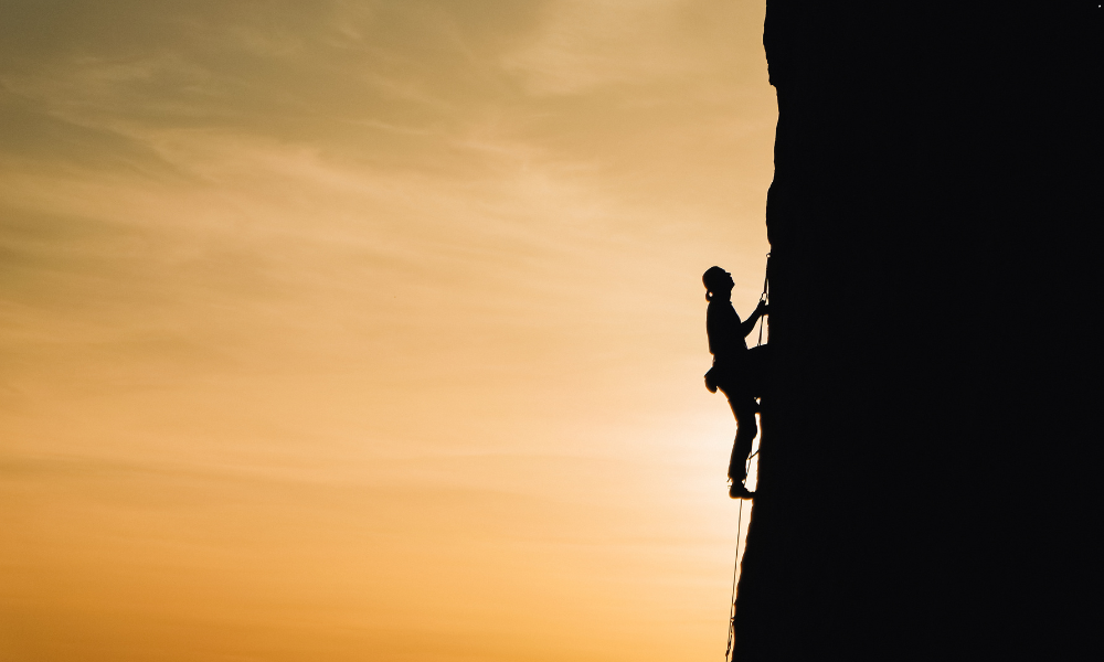 A person climbing a mountain trail at sunrise, representing steady progress and the power of consistency